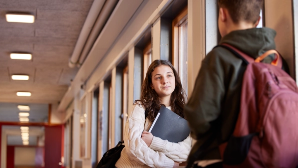 En kvinna i vit tröja och brunt hår pratar med en man som har mörkt hår, svart jacka och vinröd ryggsäck.