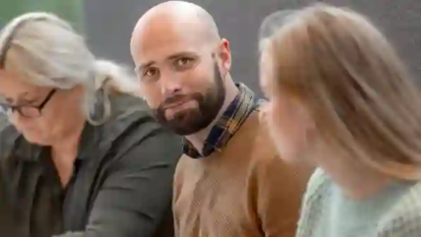 En man sitter mellan två kvinnor och tittar in i kameran.